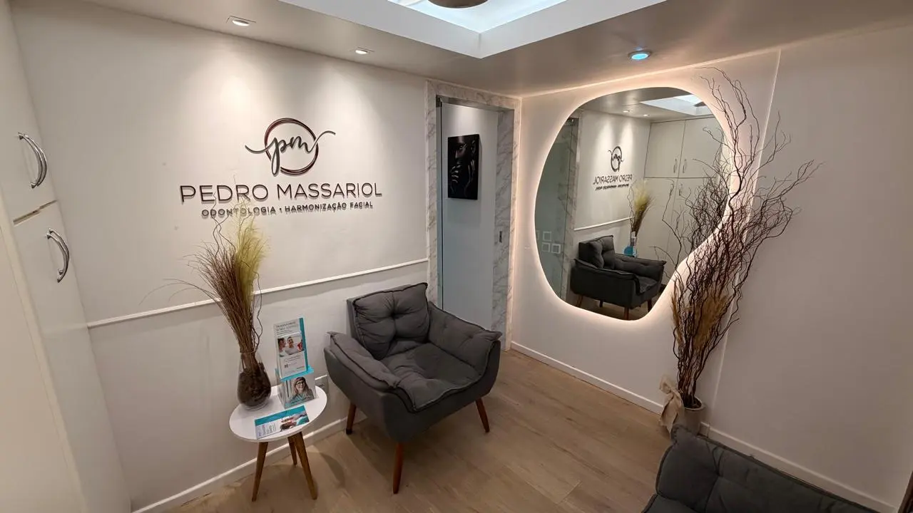 Recepção com poltrona cinza, logo Pedro Massariol na parede e espelho orgânico com iluminação